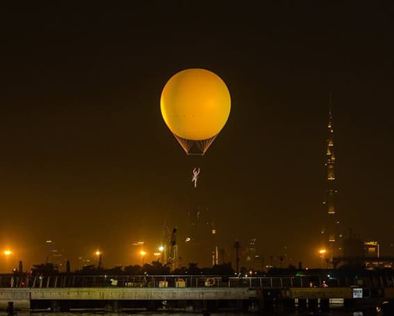 Gold-lit helium balloon carrying an aerialist high above the Dubai skyline at night