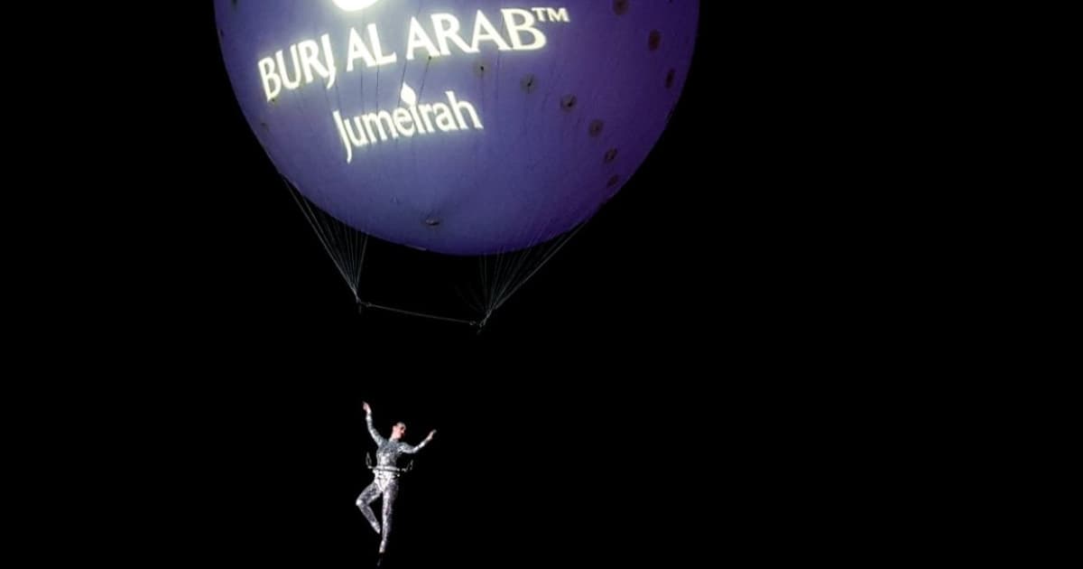 Aerialist in a mirrored silver costume suspended below a violet Burj Al Arab branded helium balloon